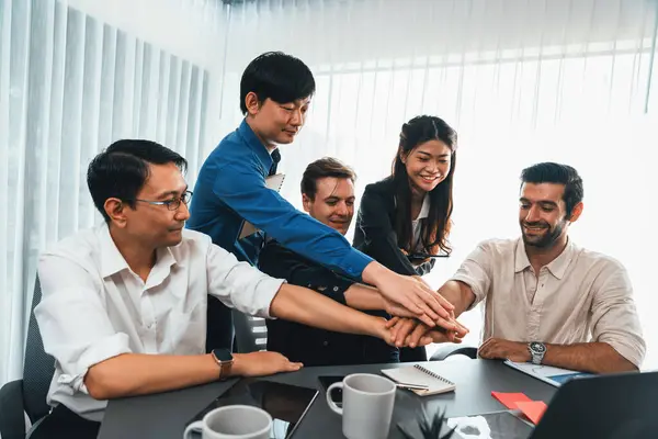 Group of diverse office worker join hand together in office room symbolize business synergy and strong productive teamwork in workplace. Cooperation and unity between business employee. Prudent
