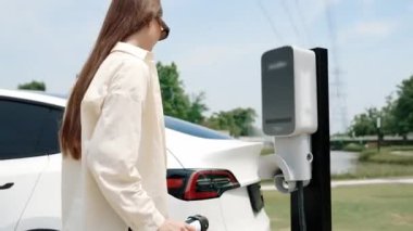 Genç kadın elektrik şebekesine bağlı elektrik şebekesine bağlı EV araba aküsünü elektrik endüstrisi olarak şarj ediyor. Çevre dostu araç kullanımı için. Yararlı
