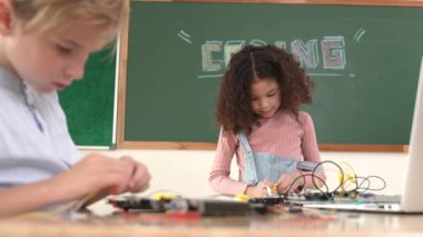 Kız tornavida kullanarak elektronik tahtayı tamir ederken ayakta duruyor. Amerikalı öğrenci ve beyaz çocuk elektrik sistemini denetlemek için birlikte çalışıyorlar. Gemide çalışan meraklı çocuklar. Pedagoji.