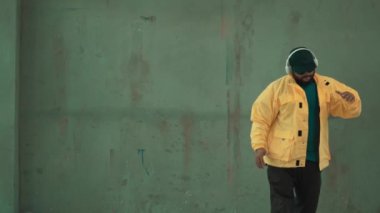 Profesyonel hipster sokak, şehir merkezinde ayak sesleri gösteriyor ya da pratik yapıyor. Genç break dansçı hareket ediyor ve kolunu ve bacağını esnetiyor. Açık hava sporu 2024. Gri arka plan. Hip hop modası. hiphop.