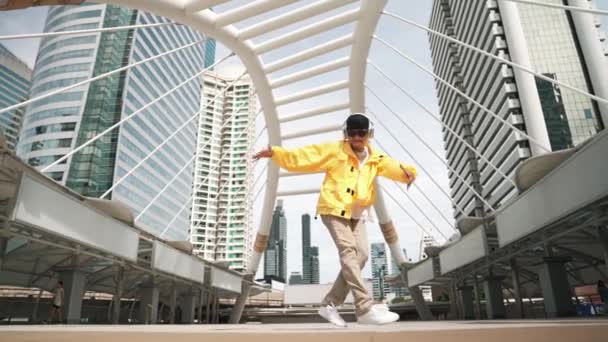 スタイリッシュなアジア人男性は低角度カメラでヒップホップダンスを行います ブレイクダンサーが階段を歩きながらヘッドフォンから音楽を聴き 街で踊っている アウトドアスポーツ 2024 スプライトリー — ストック動画
