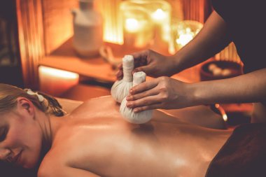Sıcak bitkisel top spa masaj vücut tedavisi, masör kadın vücuduna nazikçe şifalı bitki torbası bastırıyor. Aromaterapi tesisinin sakinliği ve dinginliği kaplıca salonundaki mumların sıcacık ışığında. Sessiz.