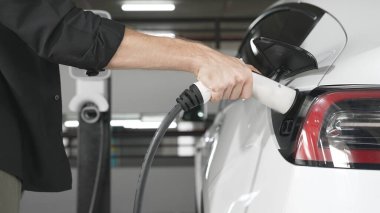 Genç adam EV elektrikli arabasıyla şehir merkezindeki alışveriş merkezinin otoparkına gidiyor şehir merkezindeki sürdürülebilirlik yaşam tarzını yeşil, temiz, yeniden şarj edilebilir elektrikli araç iç organlarıyla şarj ediyor.