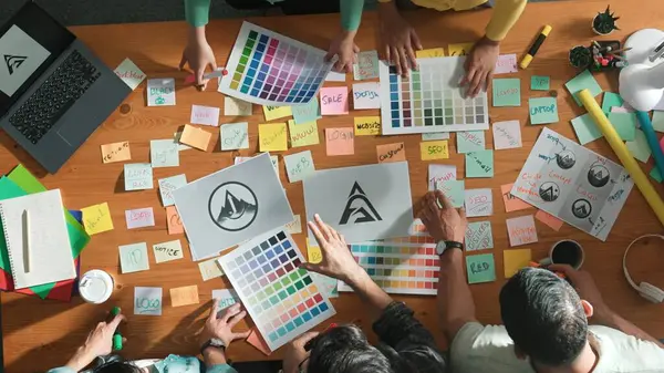 商业团队的顶视图在会议桌上写上图形标识 并附有彩色粘贴笔记和设计 同时解释想法 项目经理与聪明的团队分享想法 解释概念艺术 专题讨论会 — 图库照片