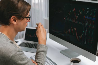 Stresli iş adamı günü modern ofisteki dinamik borsa grafiğine bakıyor, veri tabanı bilgisayarını ve bilgisayarını evden çalışırken karşılaştırıyor. Bireysel.