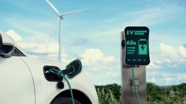 Elektrikli araba, rüzgar türbini çiftliğinde çalışan akıllı EV şarj cihazıyla şarj edilen enerjiyi şarj ediyor. Alternatif temiz sürdürülebilir enerjinin teknolojik ilerlemesi. İnceleyin