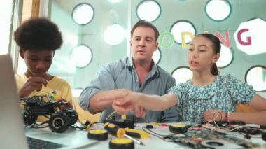 Kafkas öğrenci, öğretmene şifreyi soruyor ve bilgisayar ekranını işaret ediyor. Profesyonel eğitmen kız sorusuna cevap verirken, erkek çocuk da elektronik aletli araba modelini tamir ediyor. Öğretim