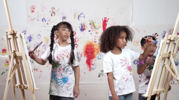 多様な学生がアートレッスンでステンドウォールで絵を描いたり キャンバスを描いたりします アジアの少女は 手のプリントでステンドウォールに立っている間 染色された色の白いシャツを着ています クリエイティブ活動 エラー — ストック動画