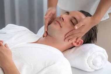Beyaz adam stres önleyici kafa masajından ve lüks bir tatil beldesi veya otel spa salonundaki modern ışık ortamında yüz güzelliği eğlencelerini şımartmaktan hoşlanıyor. Sessiz.