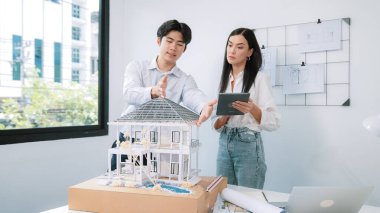 Güzel, genç, beyaz bir proje yöneticisi Asyalı mühendise, mühendislik masasında ev modelini ölçerken tablet kullanarak bina detaylarını anlattı. Tertemiz.