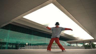 Serbest dans ederken müzik dinleyen profesyonel hipsterin hareketli çekimi. Sokak dansçısı hareket ediyor, el sallıyor ve break dansın tadını çıkarıyor. Modern yaşam tarzı. Açık hava sporu 2024. Yumuşak bir şekilde..