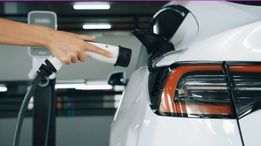 Genç adam EV elektrikli arabasıyla şehir merkezindeki alışveriş merkezinin otoparkına gidiyor şehir merkezindeki sürdürülebilirlik yaşam tarzını yeşil, temiz, yeniden şarj edilebilir elektrikli araç iç organlarıyla şarj ediyor.