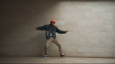 Motion of hipster gri arka planda break dans yapıyor. Sokak dansçısı hip hop hareketlerini çalışırken şık bir hip hop kıyafeti giyer ve funky müziğe yönelir. Açık hava sporu 2024. Yumuşak bir şekilde..