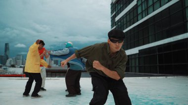 Profesyonel Asyalı dansçı B boy dansı yaparken çok kültürlü arkadaşlar çatıda dans ediyor. Genç modern dans grubu hip hop hareketi yapıyor. Tarz, moda, aksiyon. Açık hava sporu 2024. ÇalışmaComment.