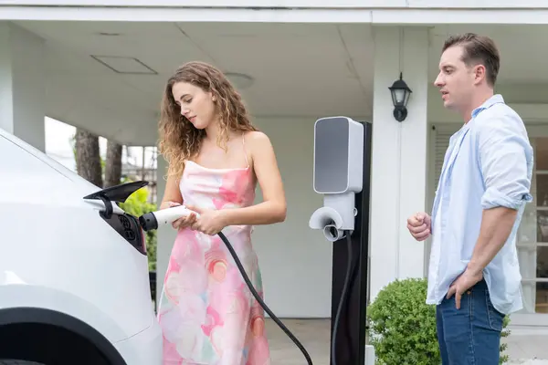 一对快乐可爱的夫妇 从电动汽车家用电器充电站购买环保的 有意识的充电电动汽车 电动汽车技术应用于住宅的未来可持续性 同步操作 — 图库照片