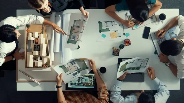 Top aerial view business people brainstorming about building interior at table with house model and laptop displayed house plan while architect engineer drawing and writing at blueprint. Alimentation.