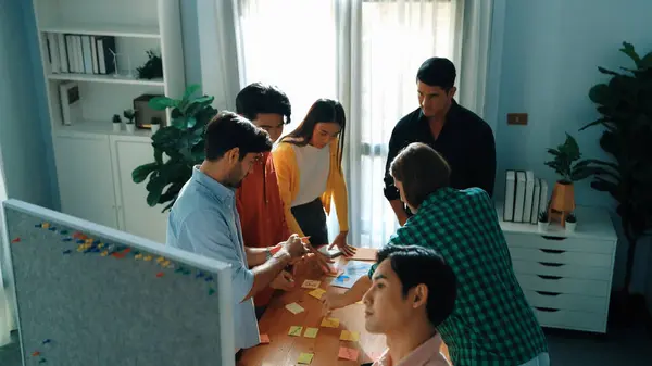 Attractive start up team brainstorming and writing marketing idea on sticky notes. Top view of diverse business people discussing while standing at boardroom. Creative business concept. Convocation.