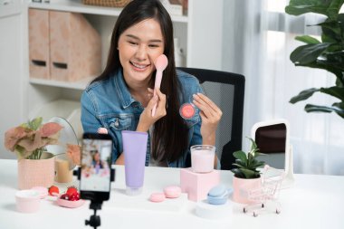 Genç, güzel Asyalı makyaj fırçası yanak testi koleksiyonunu pastel renkle inceliyor. Sosyal medyada akıllı telefonu tanıtmak için pembe ile ışıltılı bir ruh hali sergiliyor. Taktik.