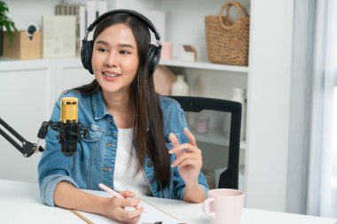 Sosyal medyada kulaklıkla canlı yayın yapan Asyalı sunucu modern stüdyoda yaşam koçluğu veya pazarlama dinleyicilerini selamlıyor. Taktik.