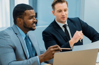 Afrikalı erkek lider stratejiyi açıklarken profesyonel proje yöneticisine çözümünü dizüstü bilgisayar kullanarak belgeye işaret ederek gösteriyor. Yetenekli iş adamlarının beyin fırtınası fikri. İş toplantısı. Süslü.