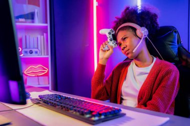 Afro-Amerikalı kız flaması, neon odada kulaklık takarak Esport yetenekli takımıyla online dövüş yaparken hayal kırıklığına uğradı. Rakiplerini kazanmak için strateji planlayan diğer oyuncularla konuşmak. Tatlandırıcı.