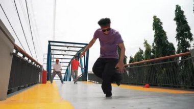 Panorama 'da hipster şık kıyafetler giyer ve dondurucu poz verir. Bir grup profesyonel dansçı break dans yaparken seçkin adam break dans yapıyor. Açık hava sporu 2024. Yumuşak bir şekilde.