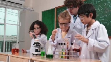 Beyaz çocuk kimyasal çözeltiyi örneğin çeşitli öğrenciler deney yaparken bırakıyor. Amerikalı bir kız, öğretmeniyle birlikte tahtada çocuklara bakarken renkli sıvıyı inceliyor. Pedagoji.