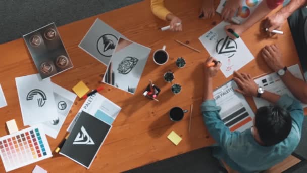 会議でロゴグラフィックをデザインするデザイナーライティングのトップビュー 着色されたパレットに取り組むビジネスマンのクローズアップと機器と紙のテーブルの上の粘着性のあるノートにアイデアを書く シンポジウム — ストック動画