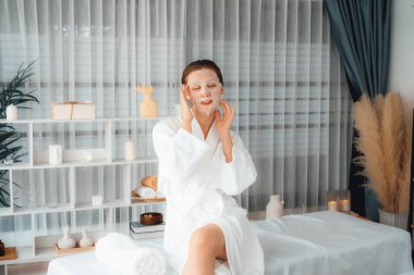 Kaplıca salonunun sakin, modern gün ışığı atmosferi, kadın müşteri poz veriyor ve yüz maskesi ile gençleştiriyor. Yüz bakımı ve güzellik kozmetolojisi prosedürü. Sessiz.