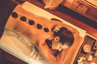 Lüks tatil köyündeki kaplıcalarda sıcak taş masajı, sıcak mum ışığı, spa bazalt taşı masajının keyfini çıkaran mutlu kadın müşteriler, rahatlatıcı bir sıcaklıkla vücudun üzerinde süzülüyorlar. Sessiz.