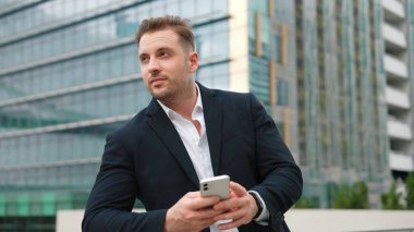 Becerikli iş adamı, çatıda dikilirken takımla sohbet etmek için telefonu kullanıyor. Pazarlama ekibiyle iletişim kurarken gökdelen görüşüyle telefonda çalışan proje yöneticisinin ön görüntüsü. Urbane.