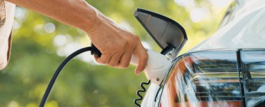 Kapanış adamı, baharda açık yeşil şehir parkındaki şarj istasyonundan elektrikli araba aküsünü şarj ediyor. Sürdürülebilir çevre dostu kentsel seyahat tarzı için şarj edilebilir EV araba. Yararlı