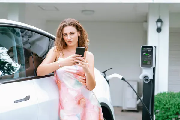 现代环保妇女从家用电动汽车充电站为电动汽车充电 创新的电动汽车技术用于跟踪能源使用情况 以优化国内的电池充电 同步操作 — 图库照片