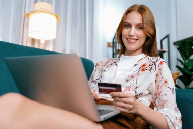 Genç mutlu kadın internetten alışveriş yaparak ürün satın alırken aynı zamanda internet üzerinden online ödeme sistemi ile çevrimiçi mağaza platformundan en yüksek siber güvenlik tarafından korunan ürünler sipariş ediyor.