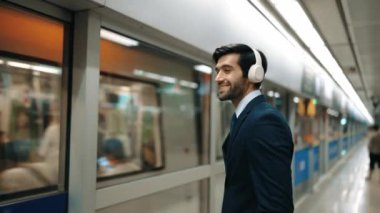Tren platformda hareket ederken akıllı proje yöneticisi kulaklıktan müzik dinliyor. Kafkasyalı iş adamı kulaklık kullanıyor. Platformda beklerken rahat müzik dinliyor. Çalışma rutini. Sevinçli..