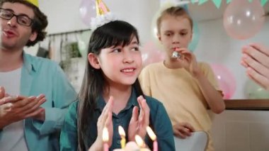 Mutlu şirin çocuk bir dilek diliyor ve doğum günü pastası mumu üflüyor. Özel bir kutlama için aile şapkası takıyor. Aile el çırparken kızların mum üfleme sahnesi. Pedagoji.