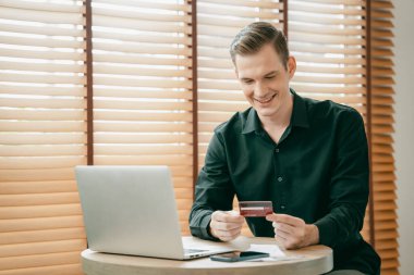 Genç adam internet bankacılığı için kredi kartlı dizüstü bilgisayar kullanıyor. İnternet üzerinden alışveriş yapıyor. Banka kartıyla modern ve kullanışlı online satın alma. Açılıyor
