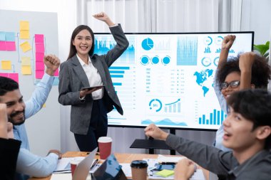 İş adamları TV ekranında başarılı bir sunum veya veri analizi toplantısından sonra kutlama yapıyorlar. Mutlu takım ofis odasında toplanıyor, kutlama jestleriyle işbirliği için tezahürat yapıyorlar. Uyum