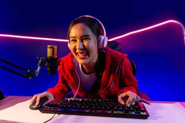 İnternet üzerinden kulaklık takıp gülümseyen Asyalı güzel kız flamasının sunucu kanalı izleyicilerle internet üzerinden konuşma yapıyor. Esport yetenekli takım oyuncuları neon mavi odada. Taktik.