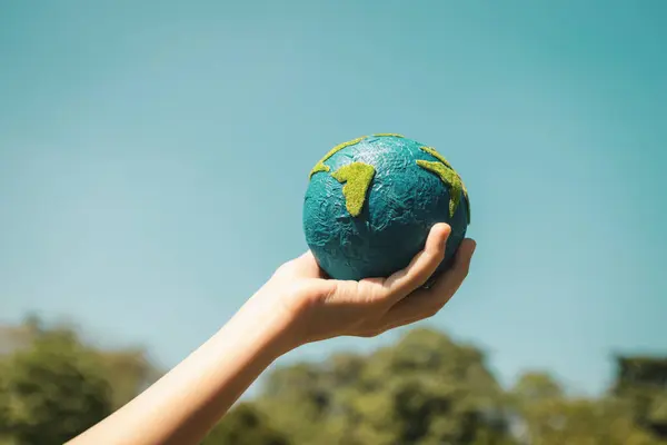 Young boys hand holding planet Earth globe with sky and cloudscape background as Earth day to save this planet with ESG principle and environment friendly energy for brighter future. Gyre