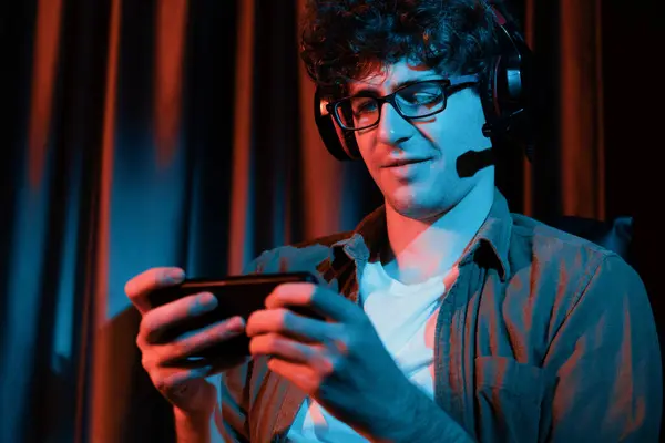 stock image Smiling young gaming streamer team playing with Esport online on smartphone fighting wearing headphones at neon light room. Practising strategy plan to win competitors for next harder level. Gusher.