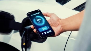 Akıllı telefon ekranı akıllı EV mobil uygulama üzerinde pil durumu EV araba garajdaki ev şarj istasyonu ile elektrik şarj ederken. Geleceğin yenilikçi EV arabası ve enerji sürdürülebilirliği. İnceleyin