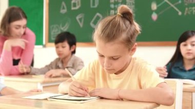 Sınıfta mutlu bir çok kültürlü öğrenci ilkokulda sınıfta sınav yaparken ya da not yazarken beyaz çocuk kameraya gülümsüyor. Eğitim konsepti. Pedagoji.