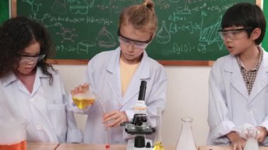 Kafkasyalı öğrenci deney yapıyor ve laboratuvarda yeni yenilikler keşfetmek için bekleyen meraklı çocuklarla çevrili biyokimyasal solüsyon döküyor. Çeşitli mutlu öğrenciler deney yapıyor. Pedagoji.