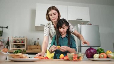 Zeki beyaz anne ve Asyalı kız birlikte yemek pişiriyor ve sebze doğruyor ya da akşam yemeği için salata hazırlıyor. Mutlu anne ve kız taze yemekle sağlıklı yemek yapıyorlar. Sağlıklı gıda konsepti. Pedagoji.
