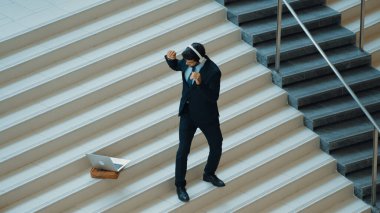 Kulaklıktan müzik eşliğinde merdivenlerde duran profesyonel bir iş adamı. Merdivenlere dizüstü bilgisayar yerleştirip dans ederken dinlenme sesi dinleyen yetenekli bir proje yöneticisi. Modern dans. Sevinçli..
