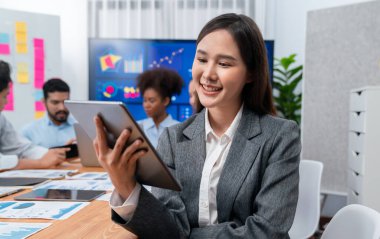 Bir grup ofis çalışanı ile birlikte arka planda ekran iş paneliyle buluşan mutlu Asyalı genç iş kadını portresi. Takım toplantısında kendine güveni tam bir ofis hanımı. Uyum