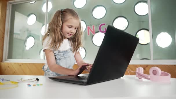 宿題をすることに集中しながら ラップトップに取り組んでいる白人少女 タイピングやゲームをしながらラップトップ画面を見ている学生 子供はテーブルの上に置かれたロボットが付いているオンライン教室に出席します エラー — ストック動画