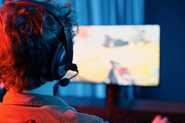 Host channel of young gaming streamer, team gamer playing battle game shooting with multiplayer at warship on pc screen with back side image, wearing headset with mic at digital neon room. Gusher. clipart