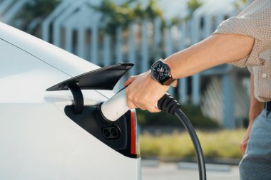 Genç adam, şehrin ticari otoparkındaki şarj istasyonundan elektrikli araba aküsünü şarj etmek için EV şarj aleti koymuş. Sürdürülebilir çevre dostu şehir yolculuğu için şarj edilebilir EV araba. Yararlı